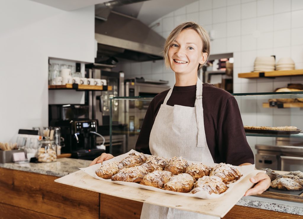 Woman in bakery holding tray of almond croissants.